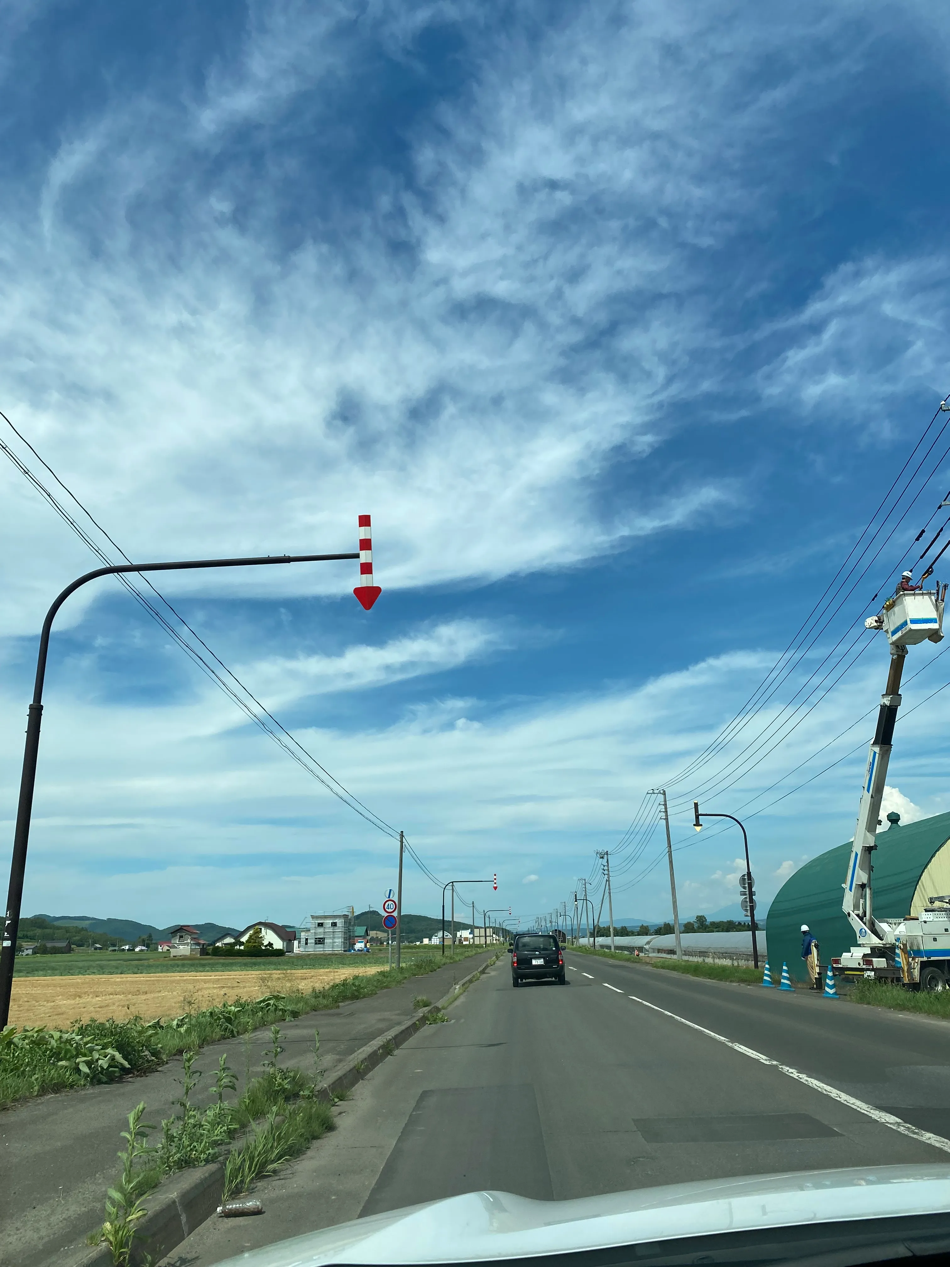 レンタカーの車内から見た郊外の道路。路肩を示す赤白の矢羽根が並ぶ